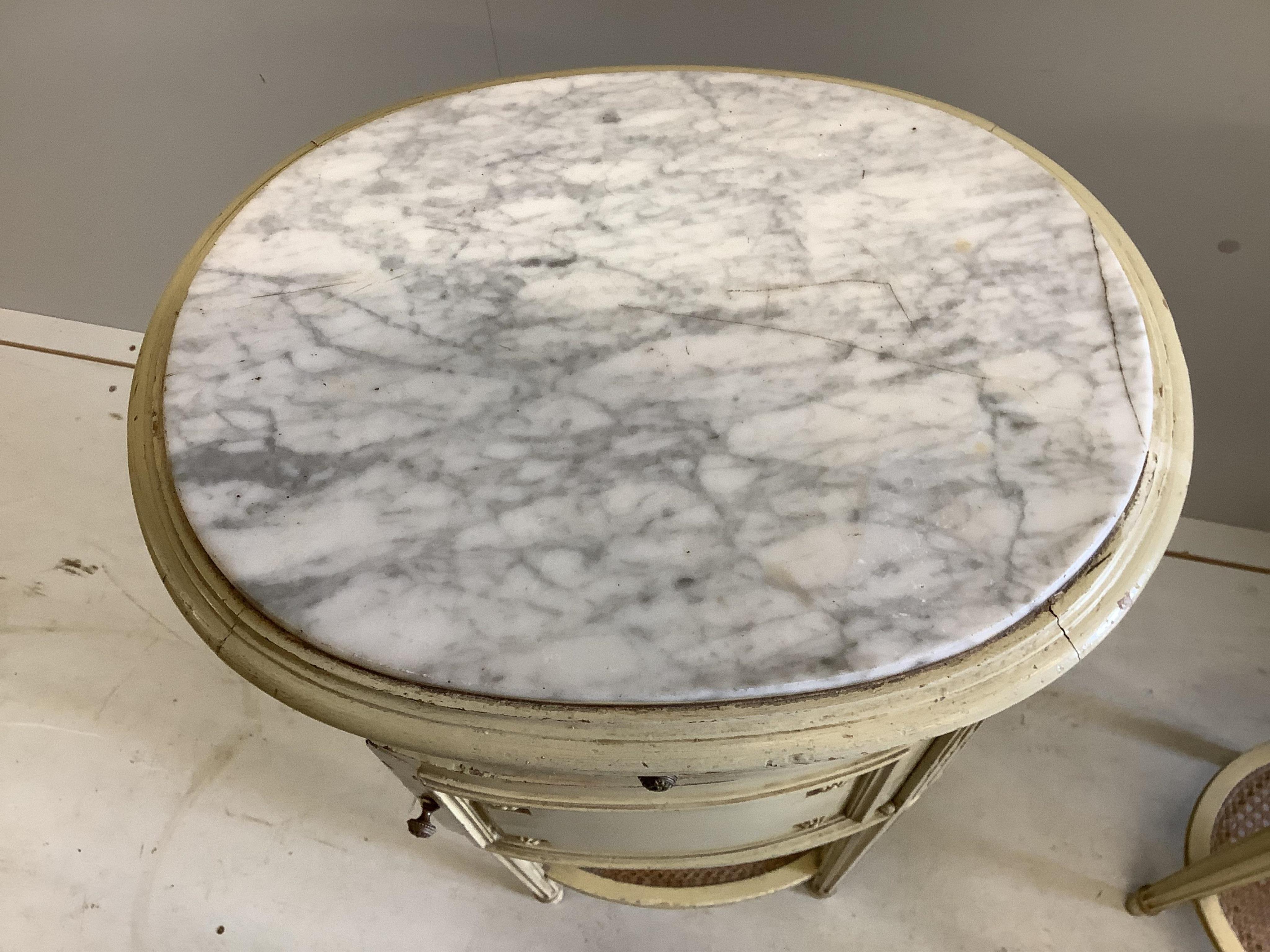 A pair of French cream painted bedside cabinets with oval marble inset tops, one fitted with a pot cupboard, width 44cm, height 83cm. Condition - fair, some differing to the marble